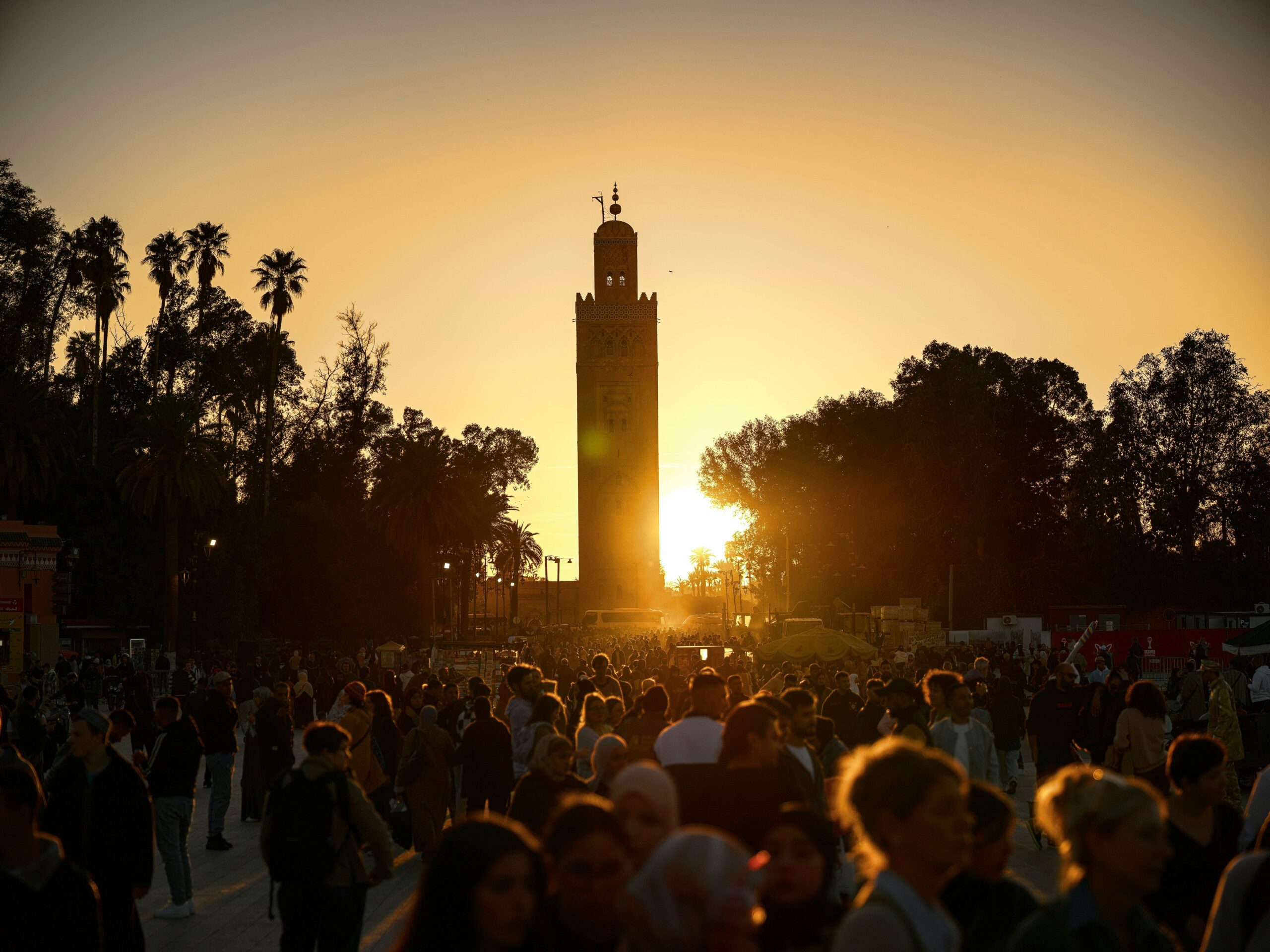 A bustling crowd gathers under the iconic Koutoubia Mosque tower at sunset in Marrakesh, Morocco.